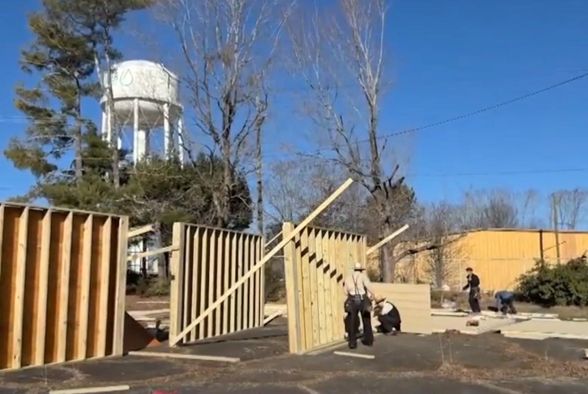 Amish or Mennonite volunteer men in straw hats and plain clothing framing the wooden walls of a small tiny home at an outdoor construction site in the North Carolina mountains, daytime, real workers visible mid-task