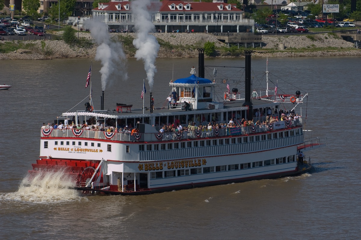 The rebuilt Belle of Louisville steamboat underway on the Ohio River, twin smokestacks steaming and decks crowded with passengers