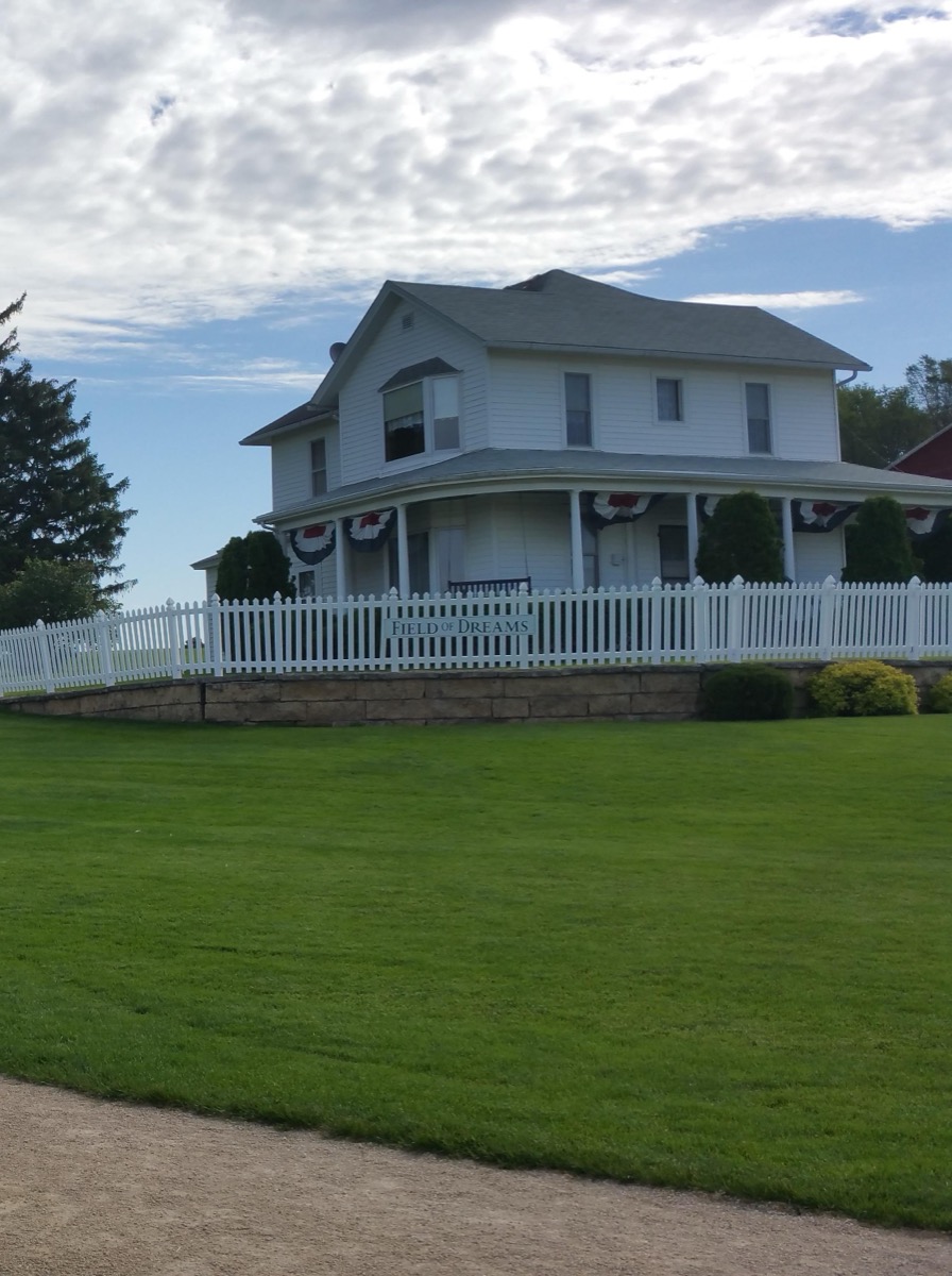 The white two-story Lansing farmhouse behind a white picket fence with a Field of Dreams sign, Dyersville, Iowa