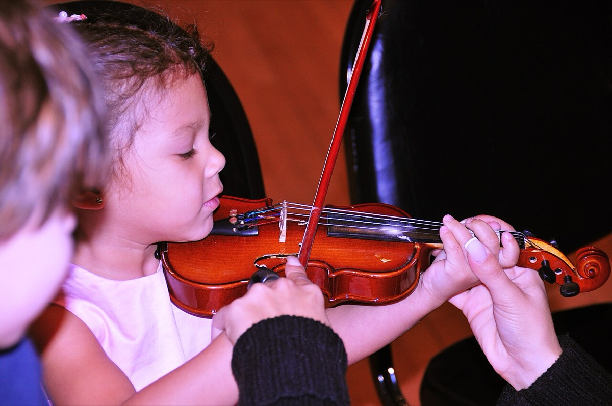 A young child receiving hands-on help learning violin from a music instructor