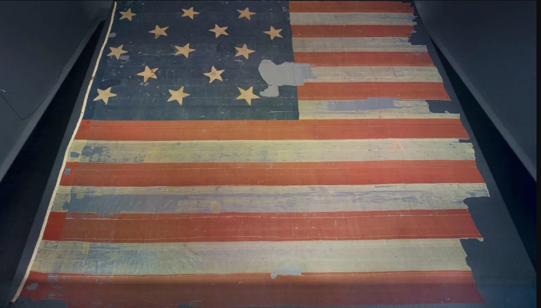 The original 1814 Star-Spangled Banner flag on display at the Smithsonian National Museum of American History, showing its worn wool bunting, 15 stars, and visible patchwork repairs