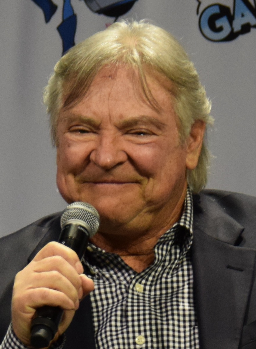 Frank Welker, the American voice actor, photographed at a fan convention or industry panel - an older white-haired man in a shirt, seated or standing at a microphone, clear head-and-shoulders framing, 2010s or later
