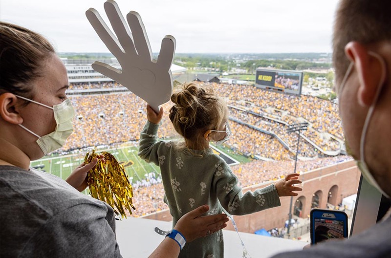 A young patient at the University of Iowa Stead Family Children's Hospital waves a foam Hawkeye hand down at the packed Kinnick Stadium crowd