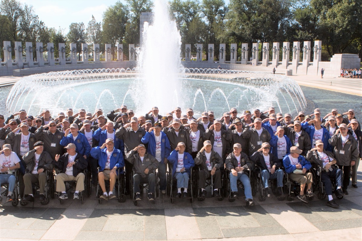 Wide daytime shot of the National World War II Memorial in Washington, DC, with visiting veterans and their guardians walking among the fountains and pillars