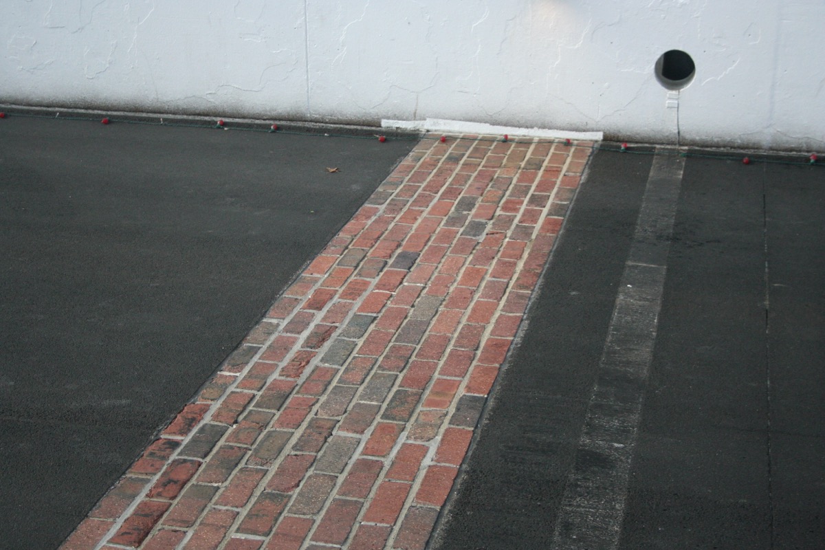 Close-up of the permanent 36-inch strip of exposed original red brick at the Indianapolis Motor Speedway start-finish line, flanked on both sides by modern black asphalt