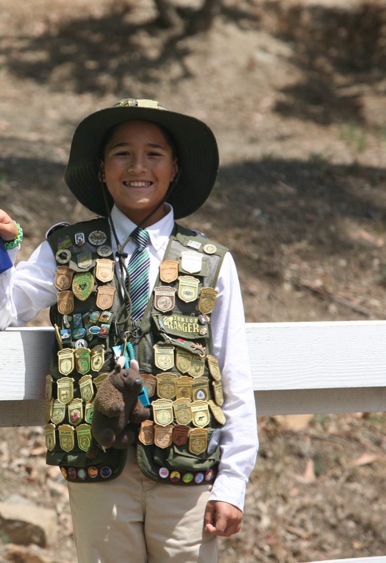 A Junior Ranger proudly wears a vest covered in dozens of earned National Park Service badges from parks across the country