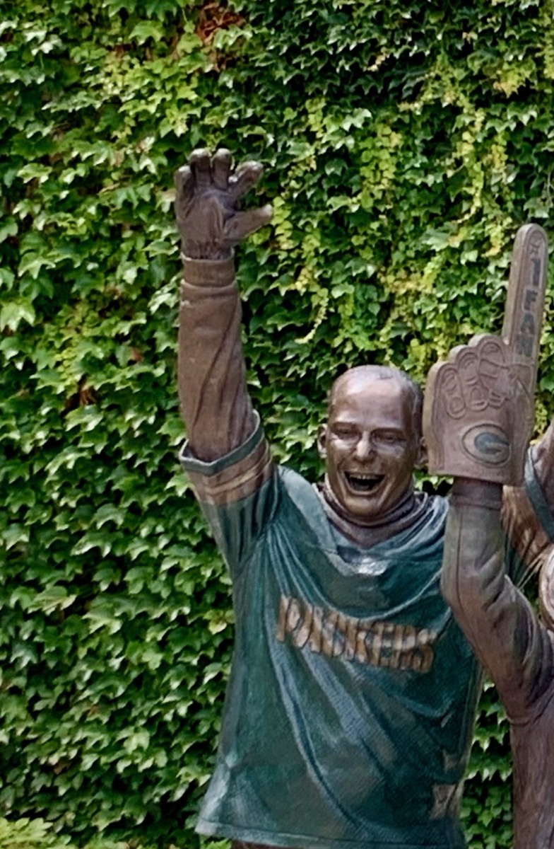 The Lambeau Leap bronze statue outside Lambeau Field, showing a Packers player mid-leap toward fans, daytime exterior shot