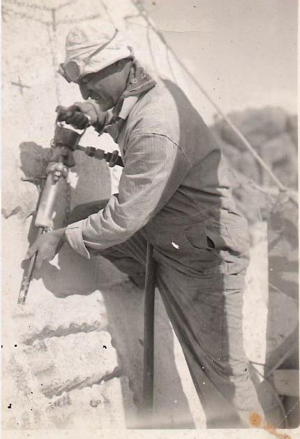 Historic black and white 1930s photo of Luigi Del Bianco at work carving stone on Mount Rushmore, close up on his hands and tools against the granite face