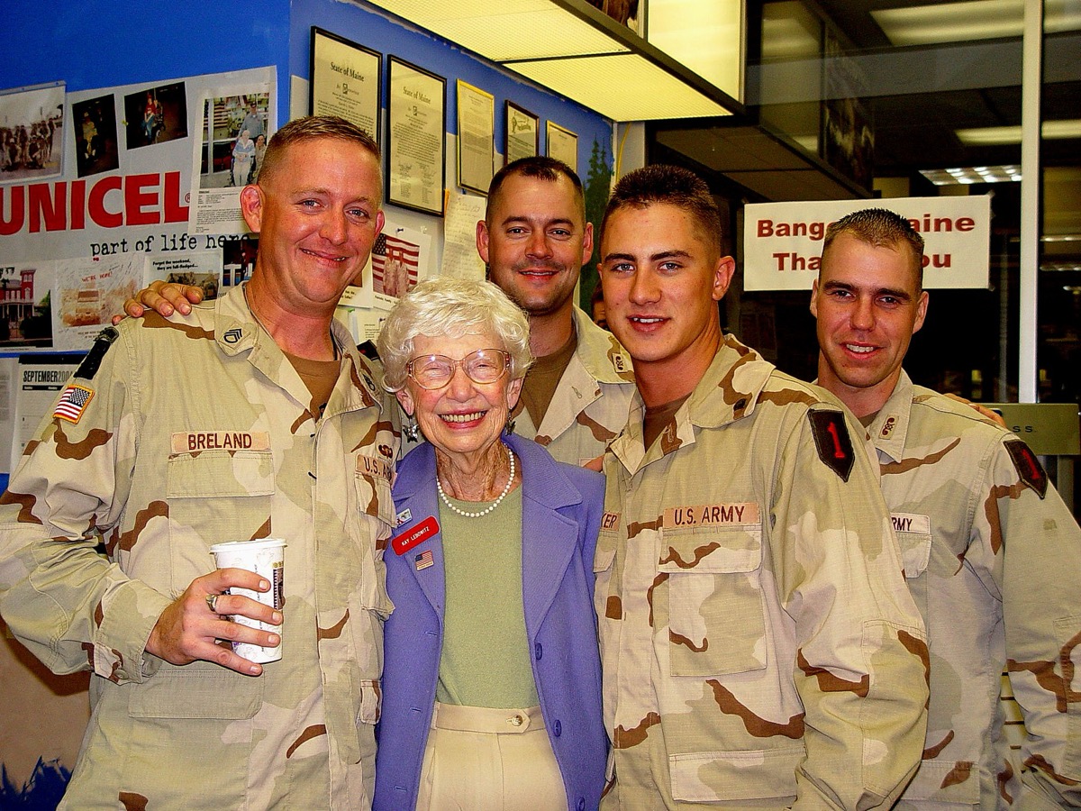 An elderly Maine Troop Greeters volunteer posing with four arriving soldiers inside the Bangor International Airport terminal