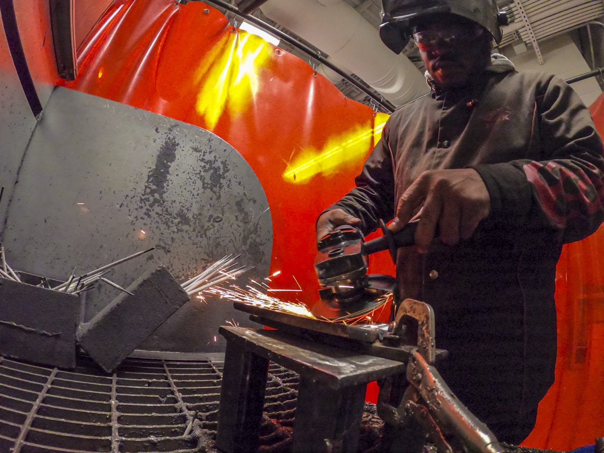 A community college student in safety gear welding in a workshop classroom, sparks visible, realistic documentary style