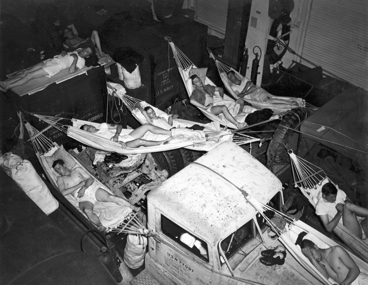 Hangar deck of a WWII aircraft carrier converted into a troop dormitory, showing rows of canvas bunks stacked several tiers high