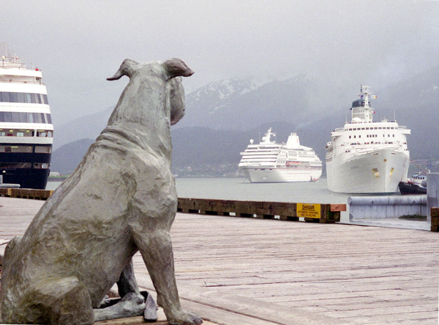 Bronze statue of Patsy Ann the bull terrier on the Juneau, Alaska wharf, facing two cruise ships arriving in the harbor