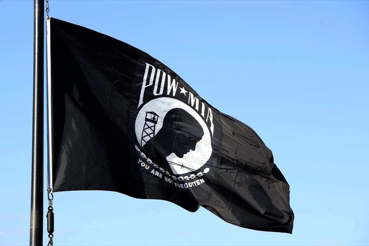 Close-up of the official POW/MIA flag artwork showing the black-and-white silhouette of a bowed head, guard tower, barbed wire, and 'You Are Not Forgotten' text
