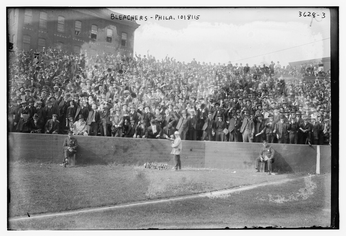 Packed bleachers at the Baker Bowl in Philadelphia on October 8, 1915, rows of fans in straw hats and flat caps behind the outfield wall during a World Series game
