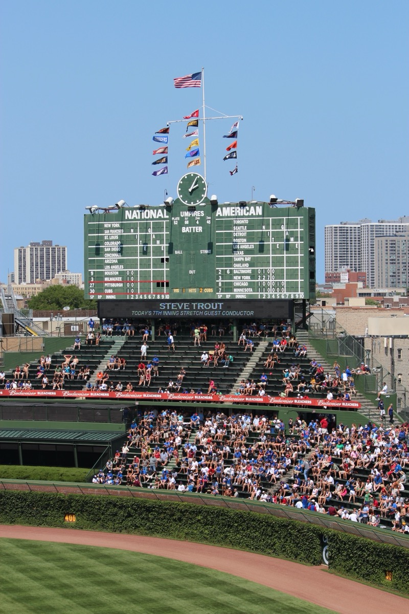 Wide view of Wrigley Field's center-field scoreboard towering above the outfield bleachers, showing its height and position relative to the playing field