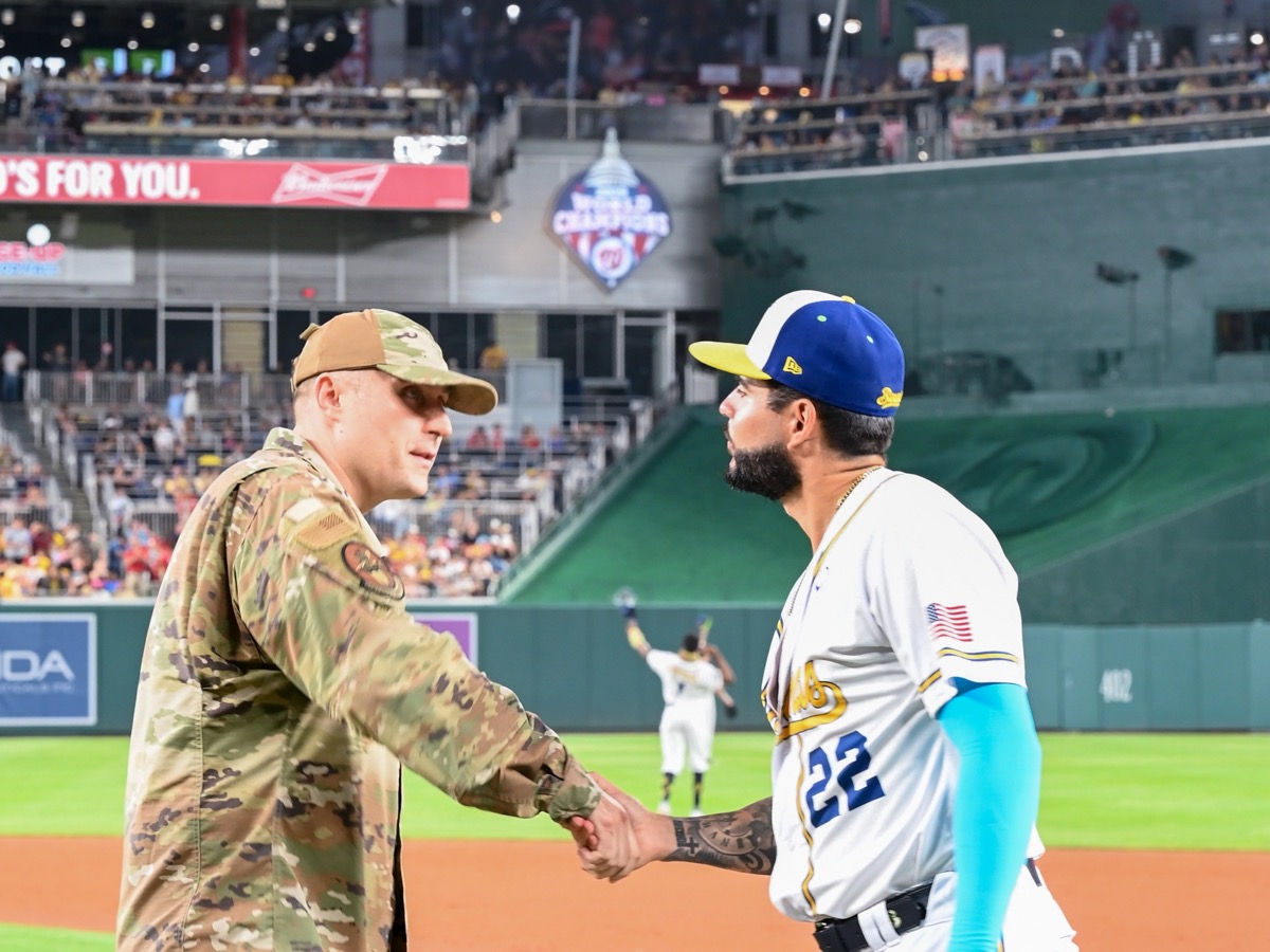 A Savannah Bananas player shakes hands with a D.C. Air National Guard member on the field at Nationals Park, a packed, sold-out Major League Baseball crowd filling the stands behind them